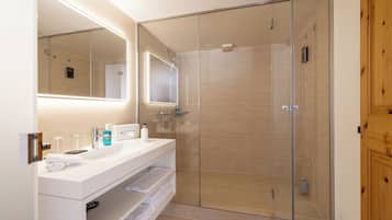 Une salle de bain moderne avec une douche à parois de verre, un meuble-lavabo blanc avec un miroir et une porte en bois.
