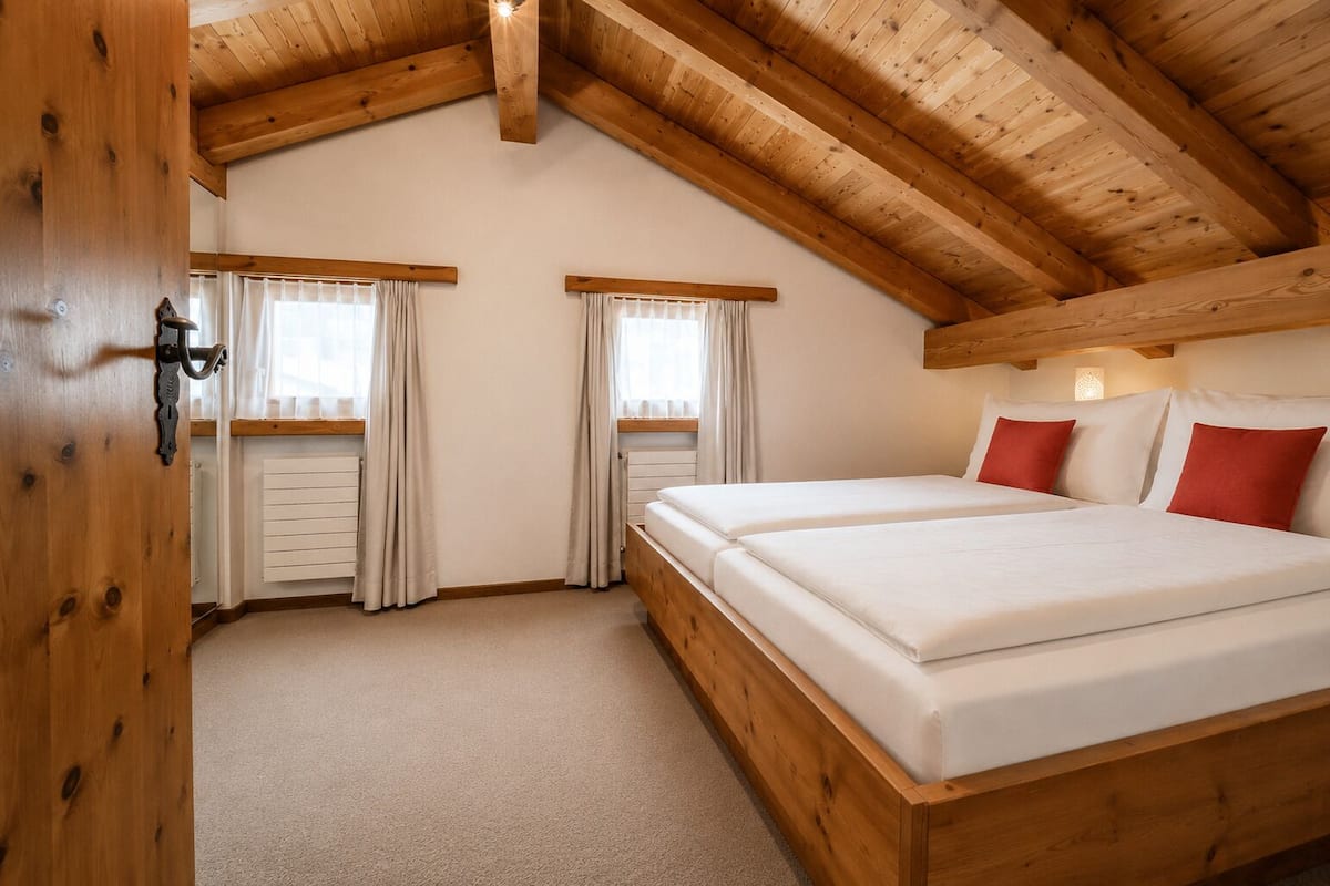 Une chambre avec un plafond en bois, deux lits, du linge de lit blanc et des rideaux.