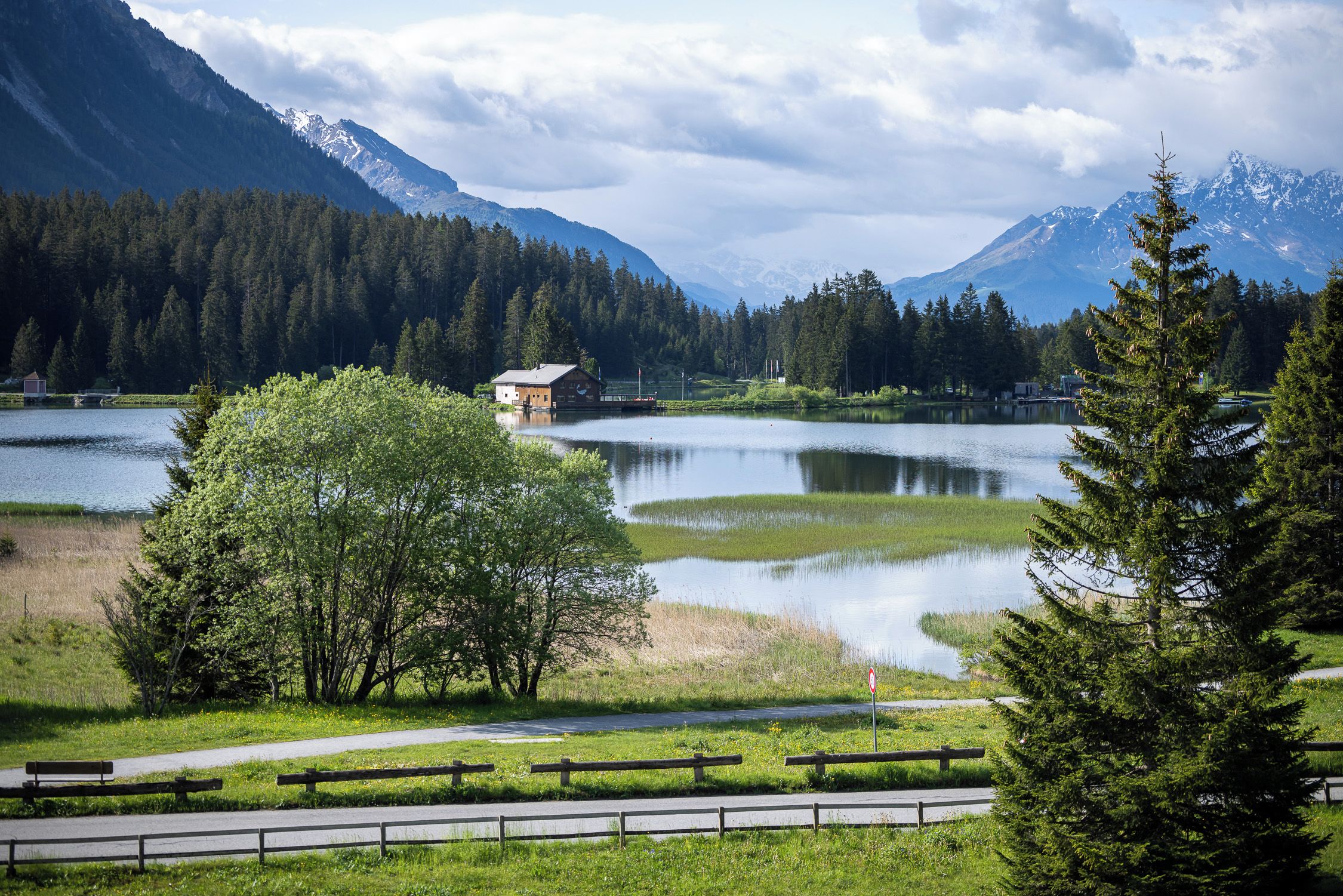 Blick auf einen See mit einer Hütte, bewaldeten Bergen und klarem Himmel.