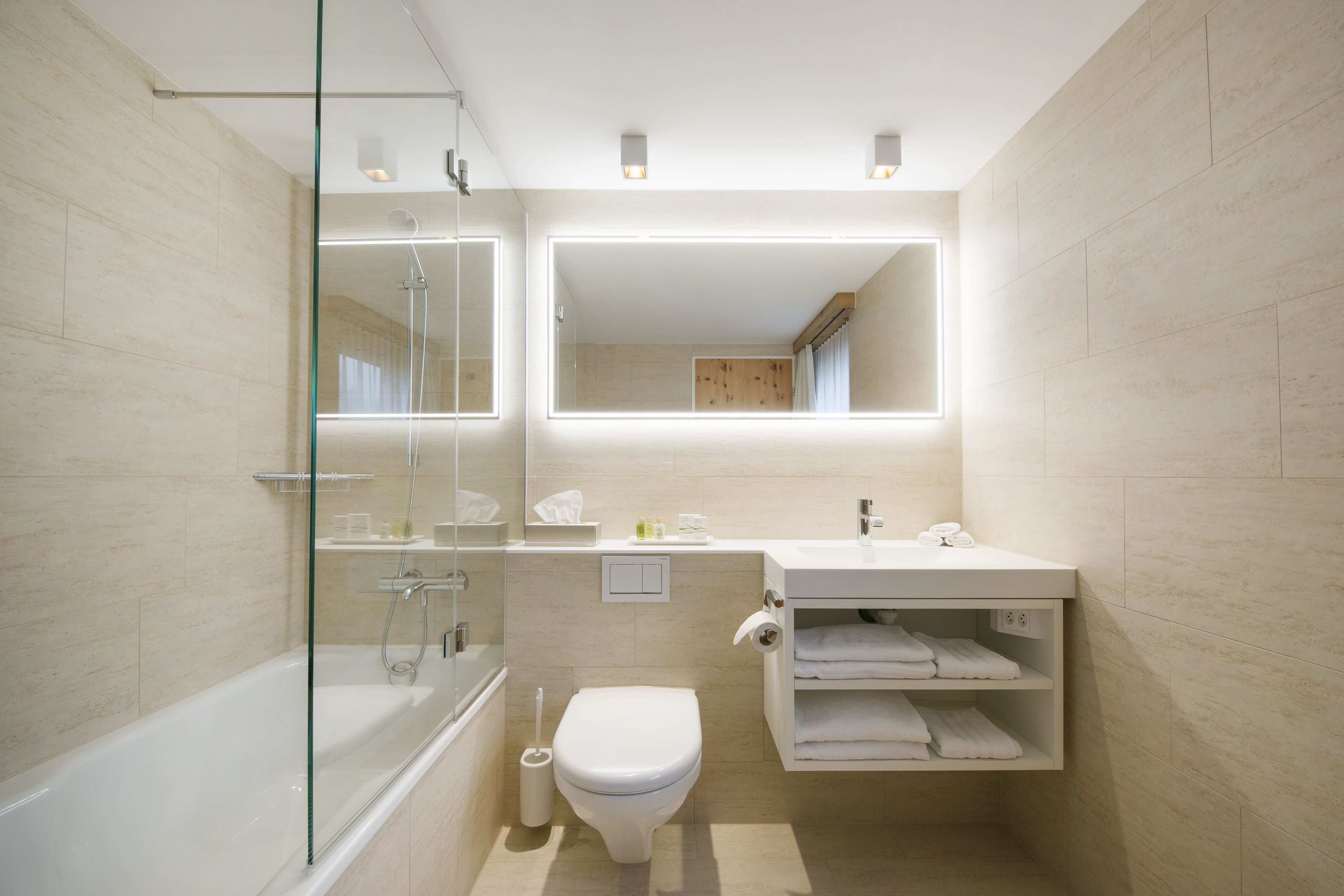A modern bathroom with a glass-enclosed shower, a white toilet, a sink with a mirror above, and a towel rack.