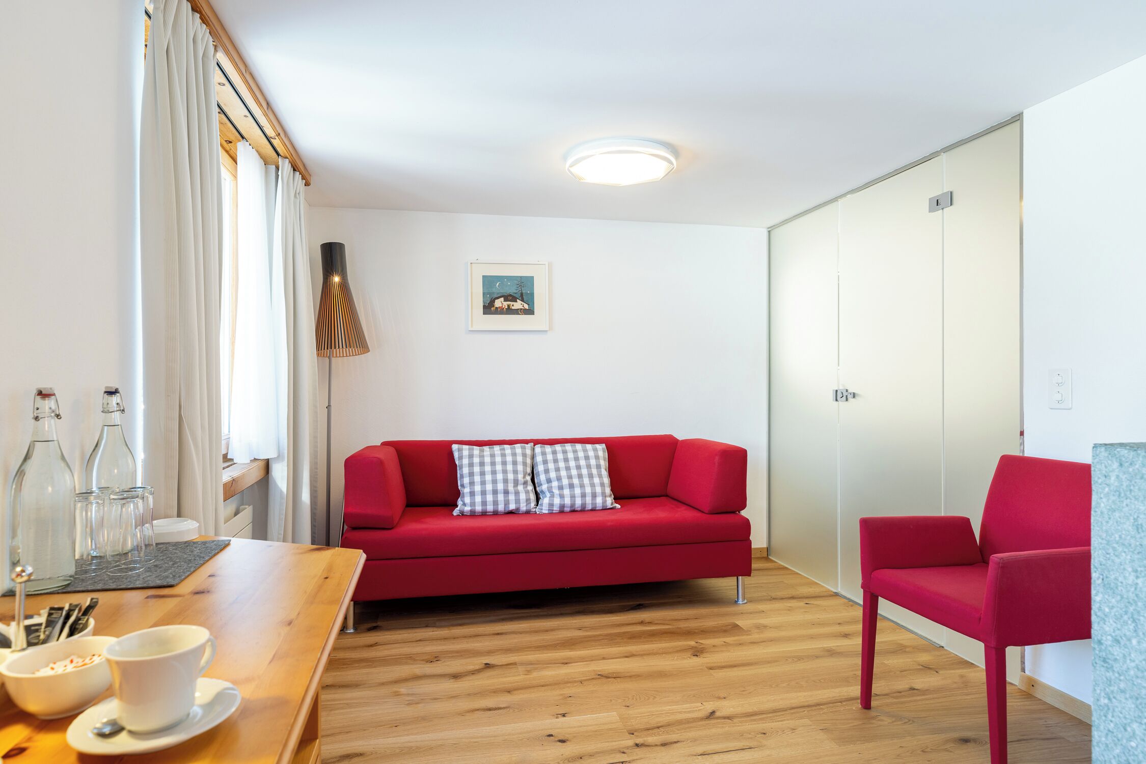 A room with a red sofa, a wooden table with a white cup and saucer, and a red chair.