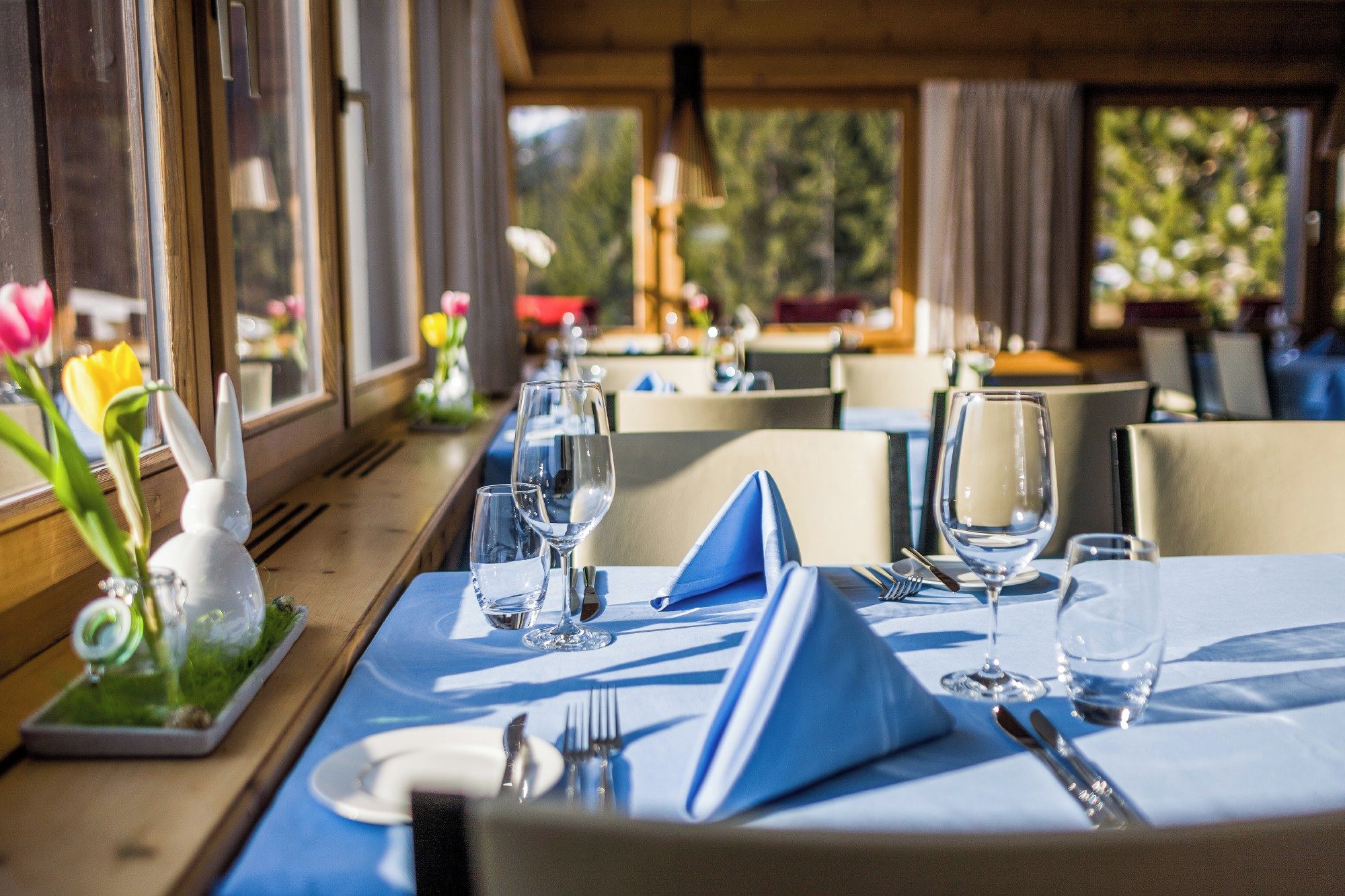 Une salle à manger de restaurant avec des tables préparées pour deux personnes, ornées de nappes bleues et de serviettes blanches.