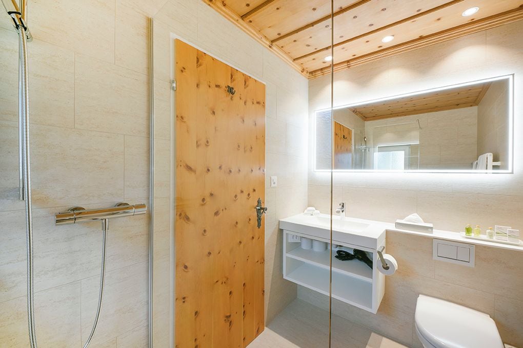 Un baño moderno con puerta de madera, cabina de ducha de vidrio y tocador blanco con espejo.