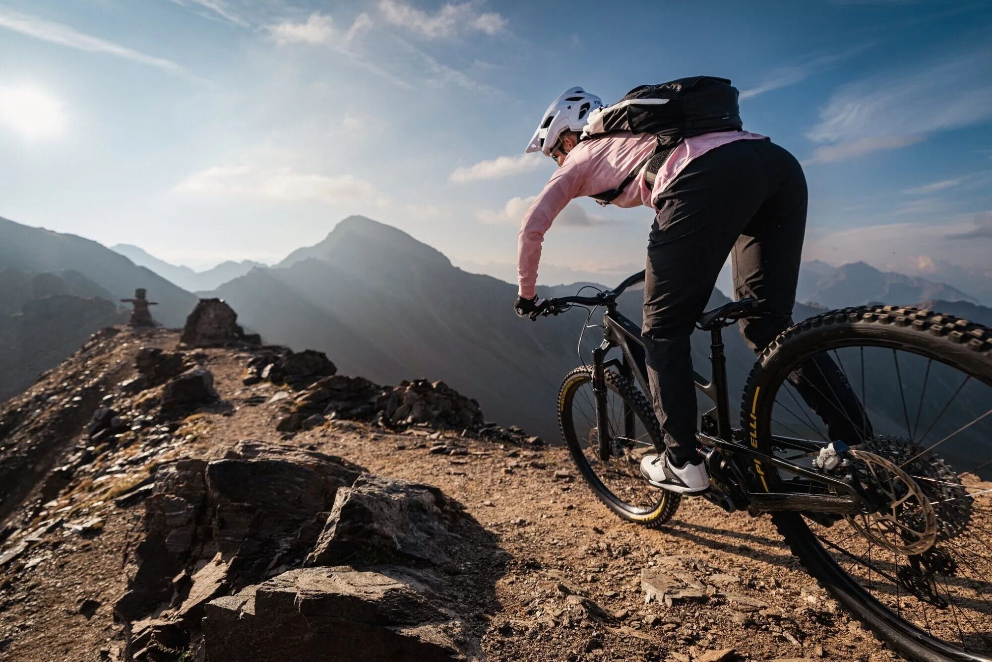 A mountain biker on a rocky trail with a mountainous backdrop.