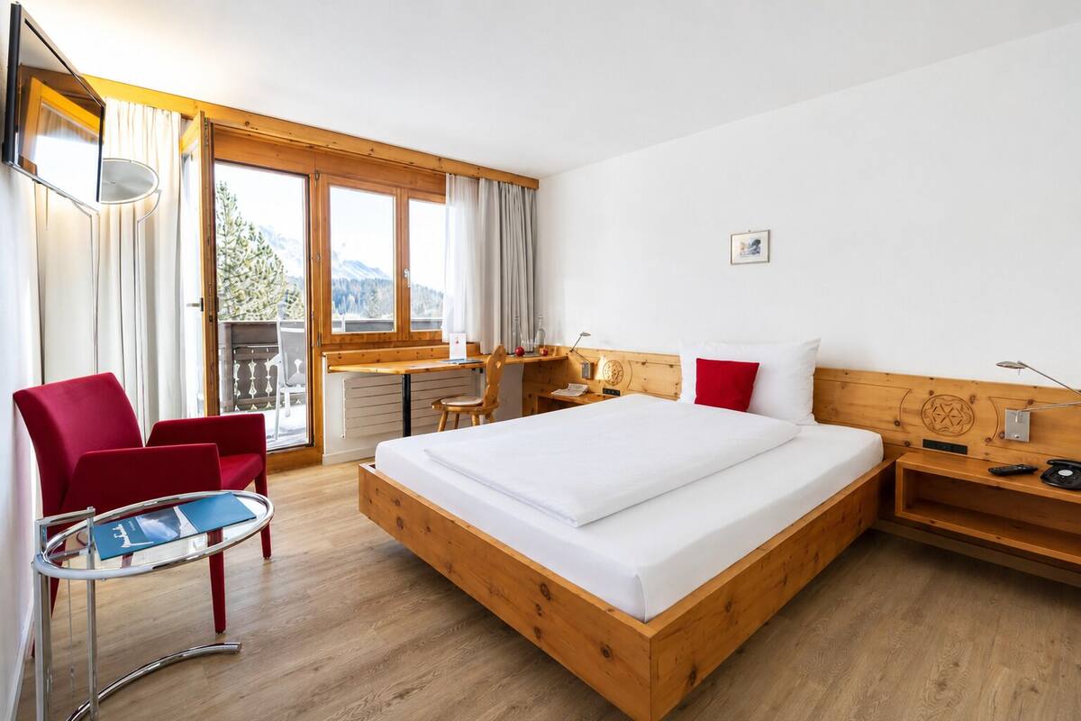 Une chambre d’hôtel avec un lit en bois, un bureau, une chaise et un balcon avec des rideaux.