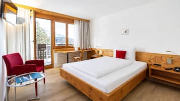 A hotel room with a wooden bed, a desk, a chair, and a balcony with curtains.