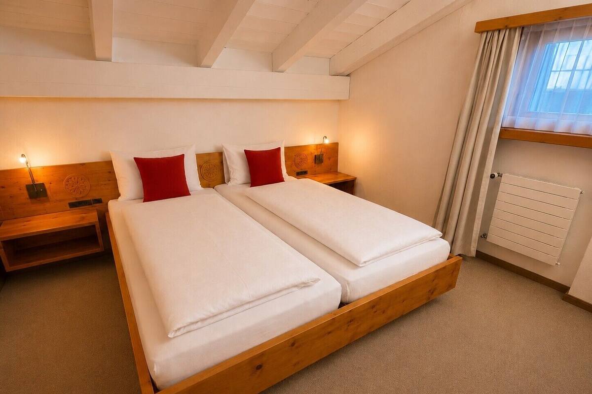 Un lit double avec une tête de lit en bois, deux tables de chevet avec des lampes, un radiateur et une fenêtre avec des rideaux.