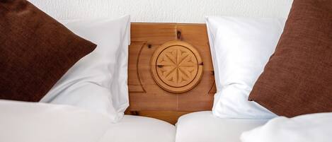 Una cama con ropa blanca y dos almohadas marrones, un cabecero de madera con diseño circular y una pared blanca con textura de fondo.