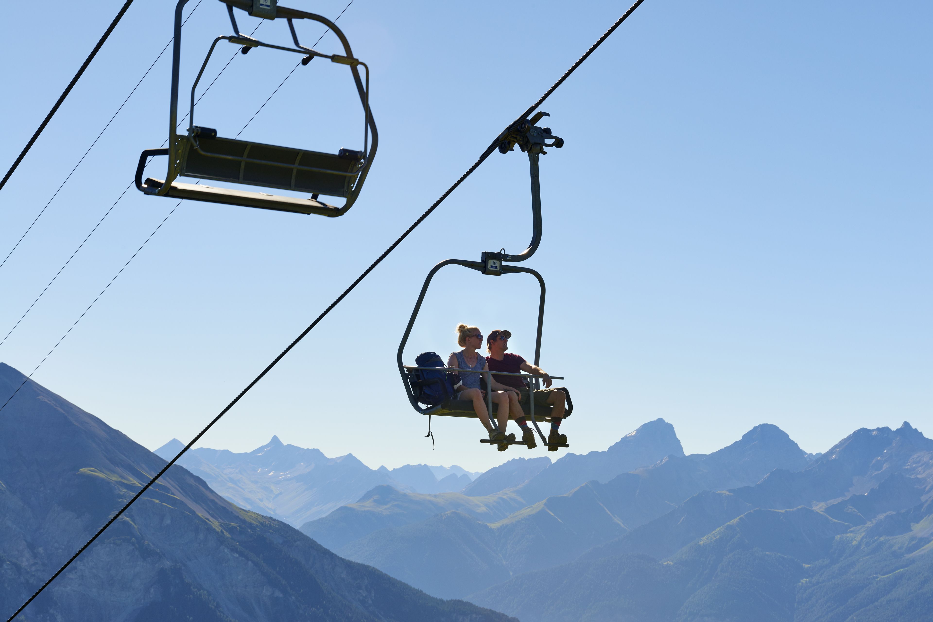A cable car with passengers, set against a backdrop of mountains.