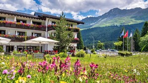 A hotel with balconies adorned with flowers, outdoor seating, and a view of mountains.
