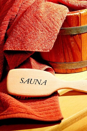 A wooden spa brush labeled "SAUNA" on a red towel, with a wooden chest in the background. - Penzion Slatina (Lipova-Lazne)