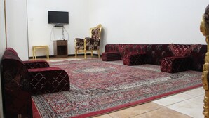 Un salon avec un canapé rouge à motifs, un fauteuil à motifs et un téléviseur fixé au mur.
