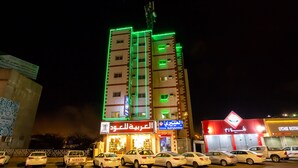 Un immeuble à plusieurs étages, doté d’une enseigne lumineuse en arabe, un parking avec plusieurs voitures et une entrée bien visible.