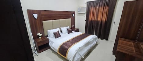 Habitación de hotel con una cama grande, cabecera de madera, mesita de noche con lámpara y ventana con cortinas.