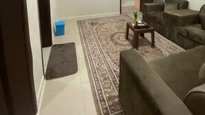 A living room with a flat-screen TV mounted on the wall, a brown sofa, a coffee table with a plant, and a patterned rug.