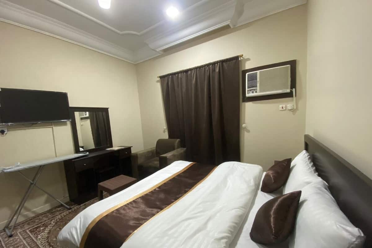 Een hotelkamer met een groot bed, een bureau met spiegel, een stoel, een klein tafeltje en een airconditioner aan de muur.