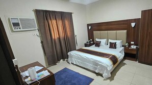 A hotel room with a bed, a desk, a chair, a nightstand, a lamp, a telephone, and a window with curtains.