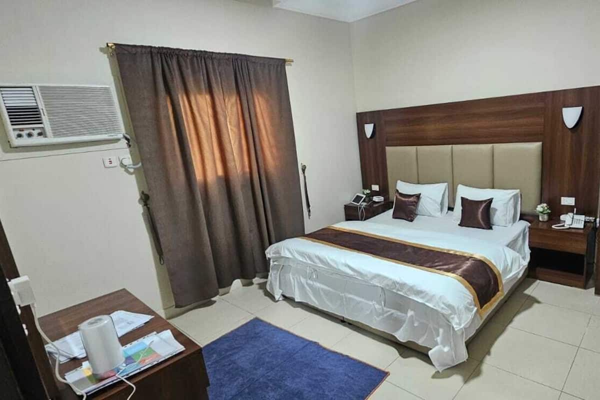 Hotelkamer met een bed, nachtkastjes, bureau, stoel, gordijn en een luchtverkoeler aan de muur.