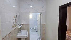 A narrow bathroom with a white sink, a toilet, and a shower area.