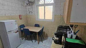 A compact kitchen with a refrigerator, a table with chairs, a window, a sink, and a stove.