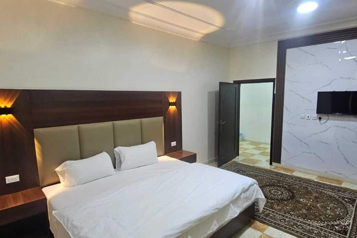 Ein Hotelzimmer mit Bett, Nachttischen, einem an der Wand montierten Fernseher und einer Wand mit Marmoroptik.