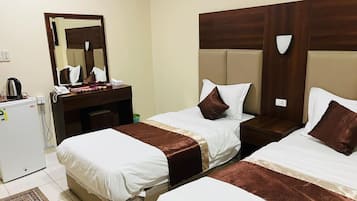 A hotel room with two beds, a desk with a telephone, a mirror, and a refrigerator.