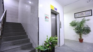 Un hall d’entrée propre et moderne, avec un escalier en marbre, un panneau d’indication concernant la sécurité incendie, une plante en pot et des œuvres d’art encadrées accrochées au mur.