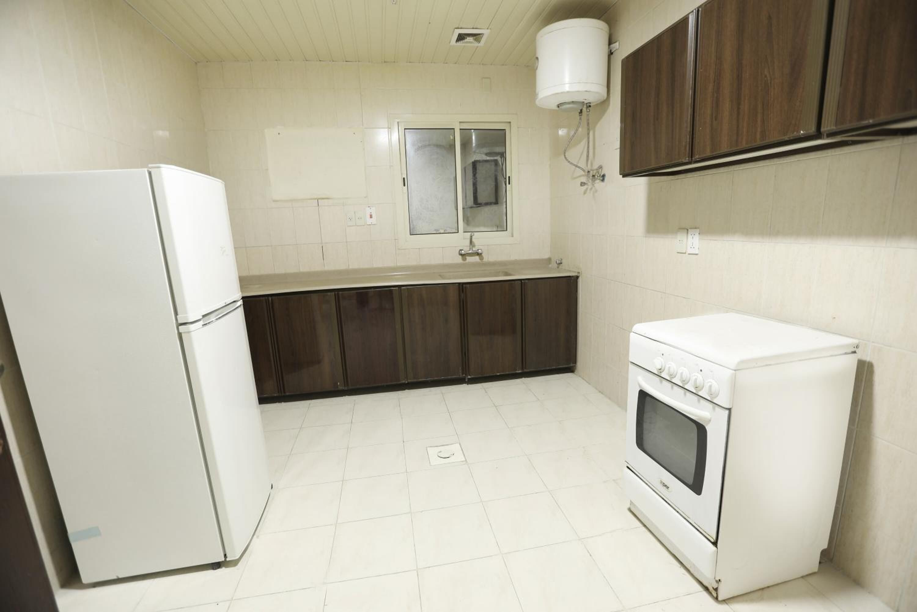 A kitchen with white appliances, wooden cabinets, and a tiled floor.