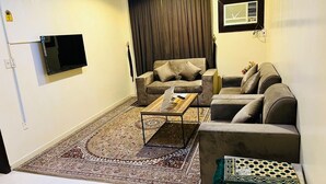 Un salon avec deux canapés, une table basse, un téléviseur fixé au mur et un tapis à motifs.