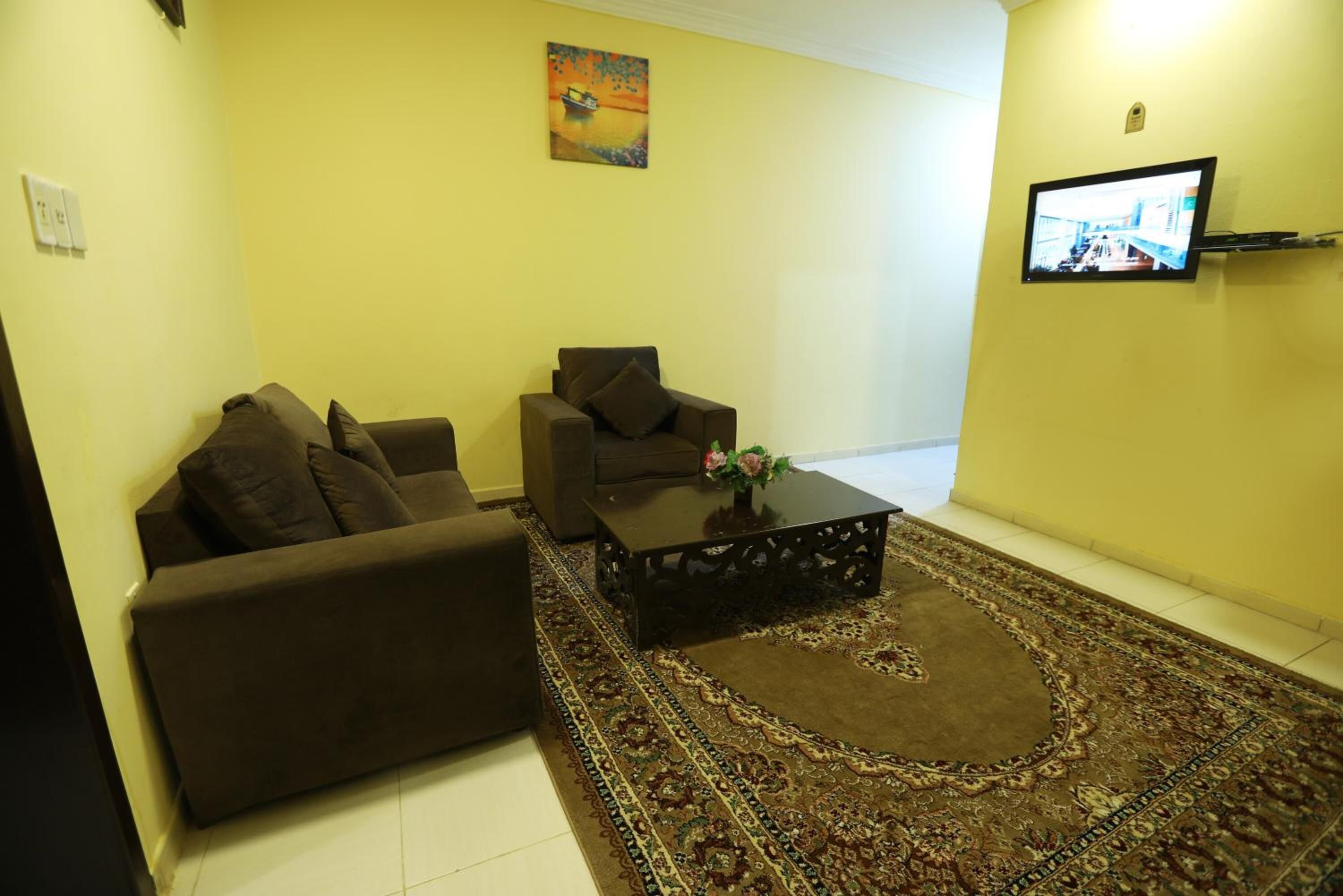 Una sala de estar con sofá, sillón, mesa de centro y televisor montado en la pared.