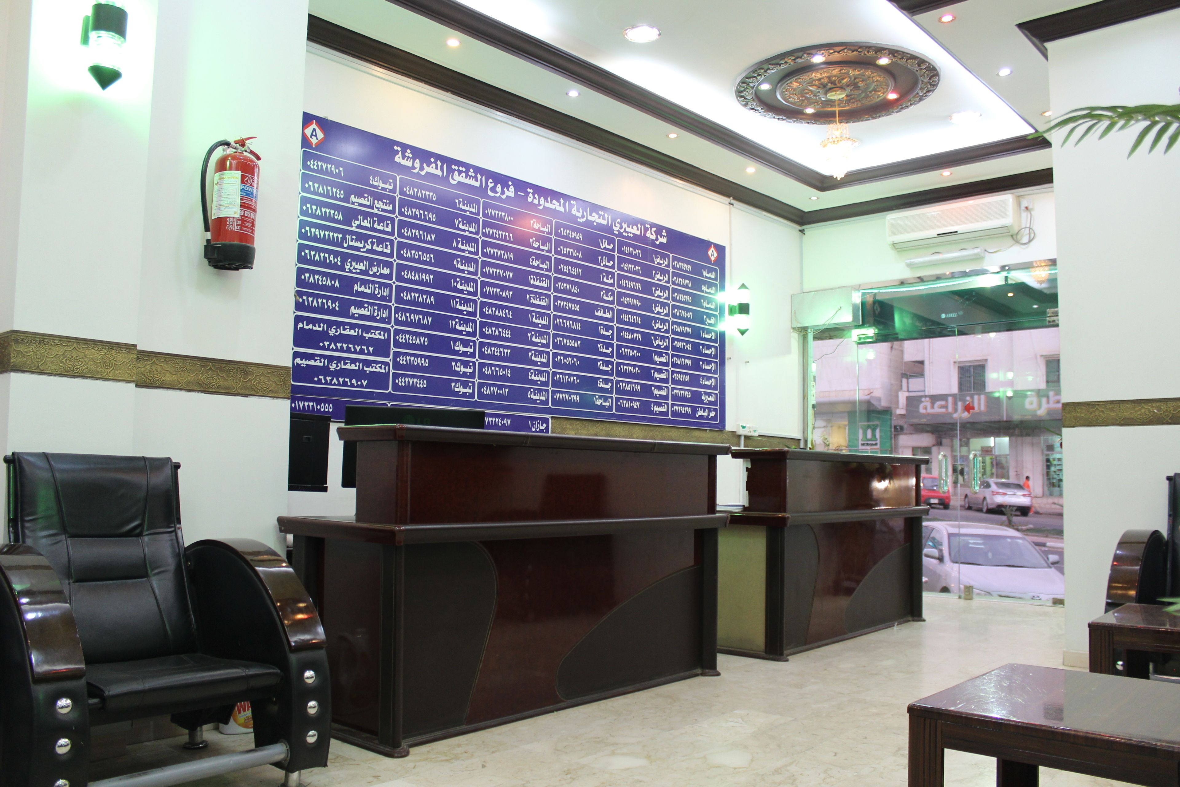 A reception area with a large directory board, a fire extinguisher, and a desk with a chair.