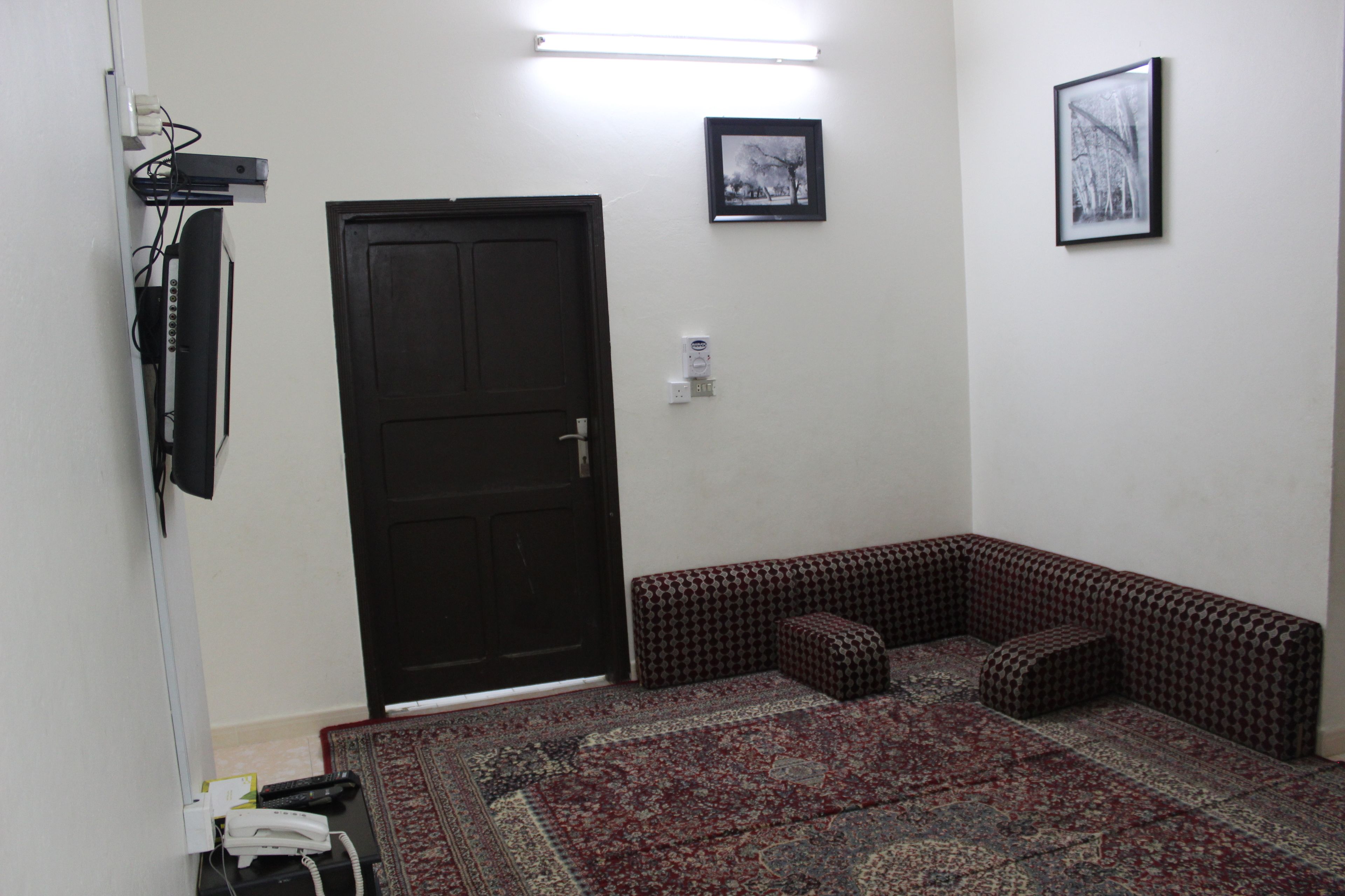 A room with a black door, a patterned rug, a bench, and a framed picture on the wall.
