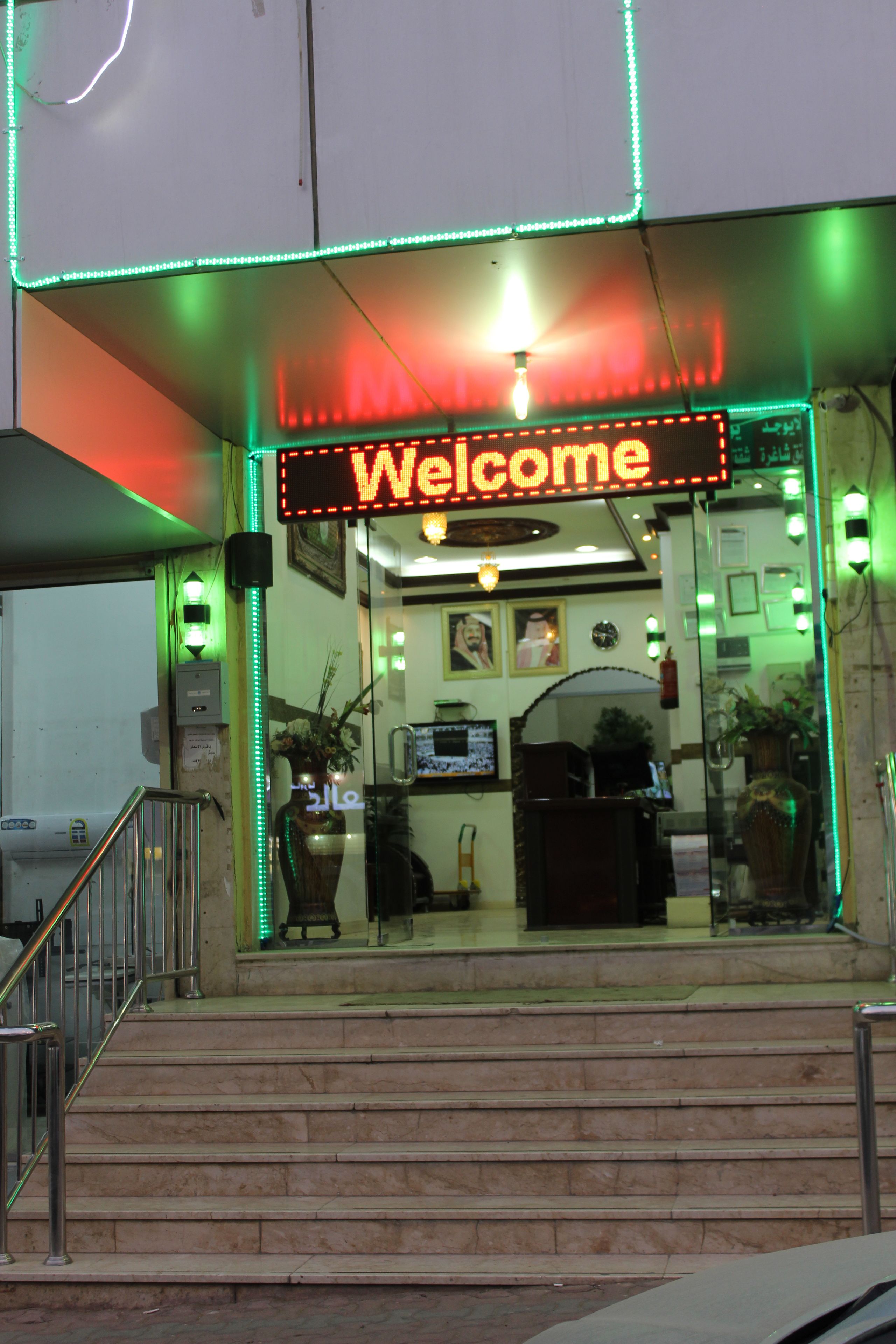 A hotel entrance with a 'Welcome' sign, a staircase, and a reception desk.