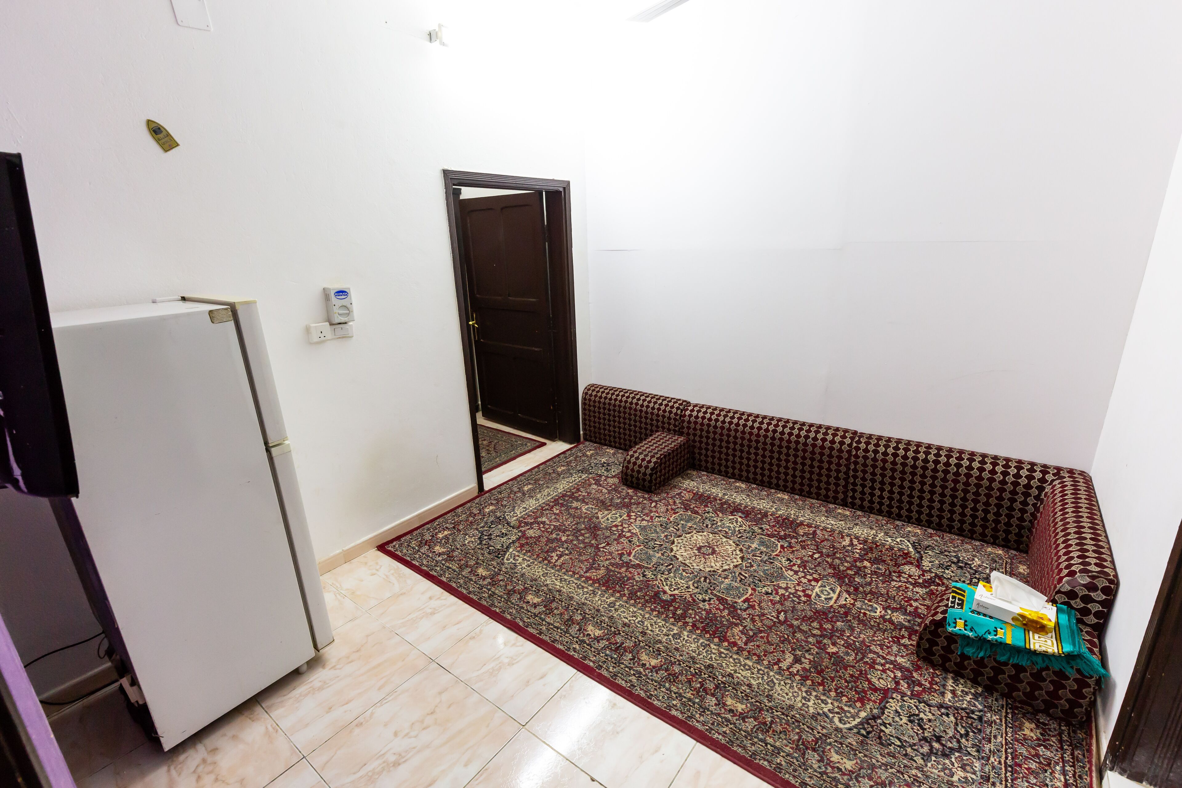 Une petite pièce, de taille modeste, avec un tapis à motifs, un canapé et un réfrigérateur.