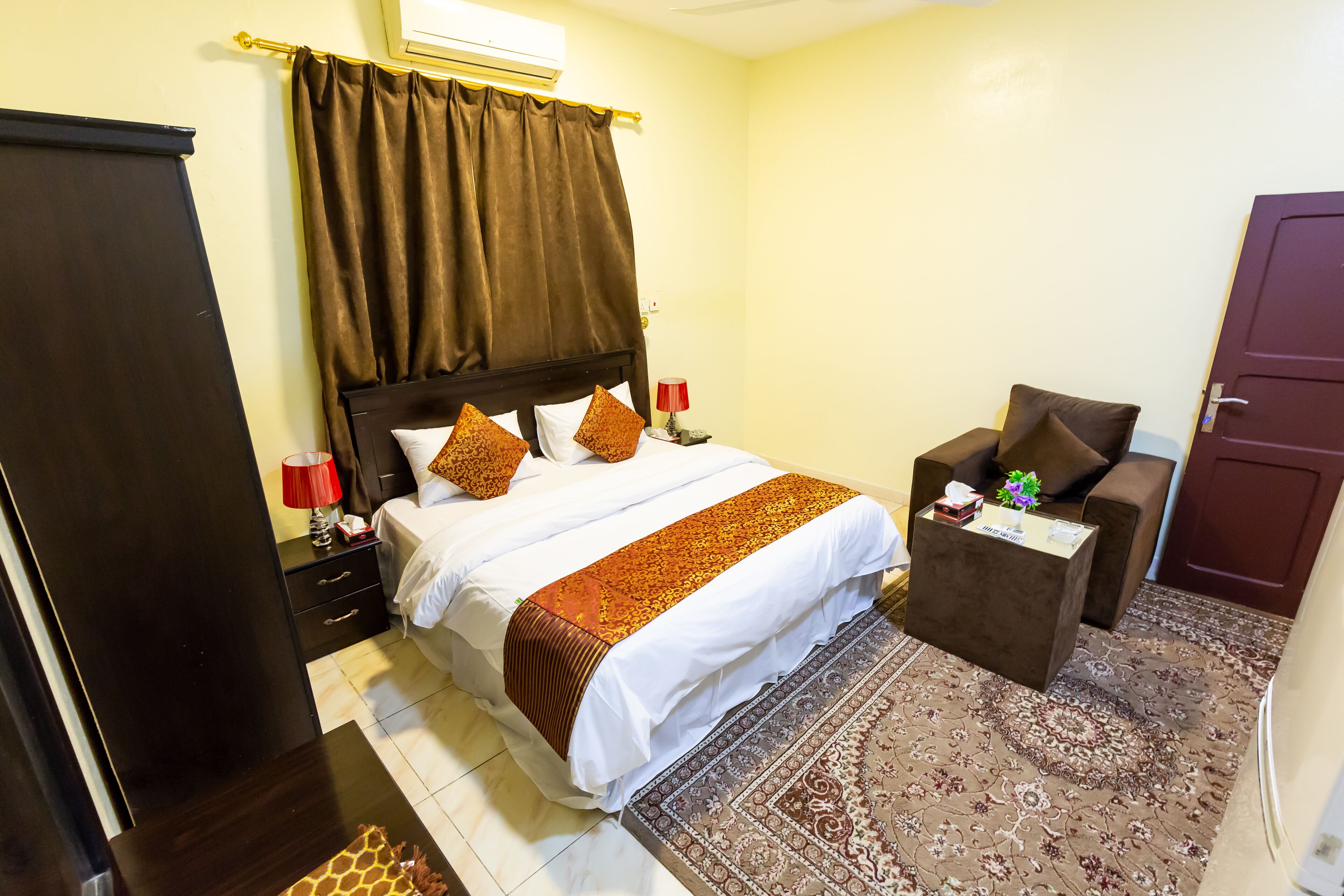 A hotel room with a bed, a nightstand, a chair, a desk, and a wardrobe.