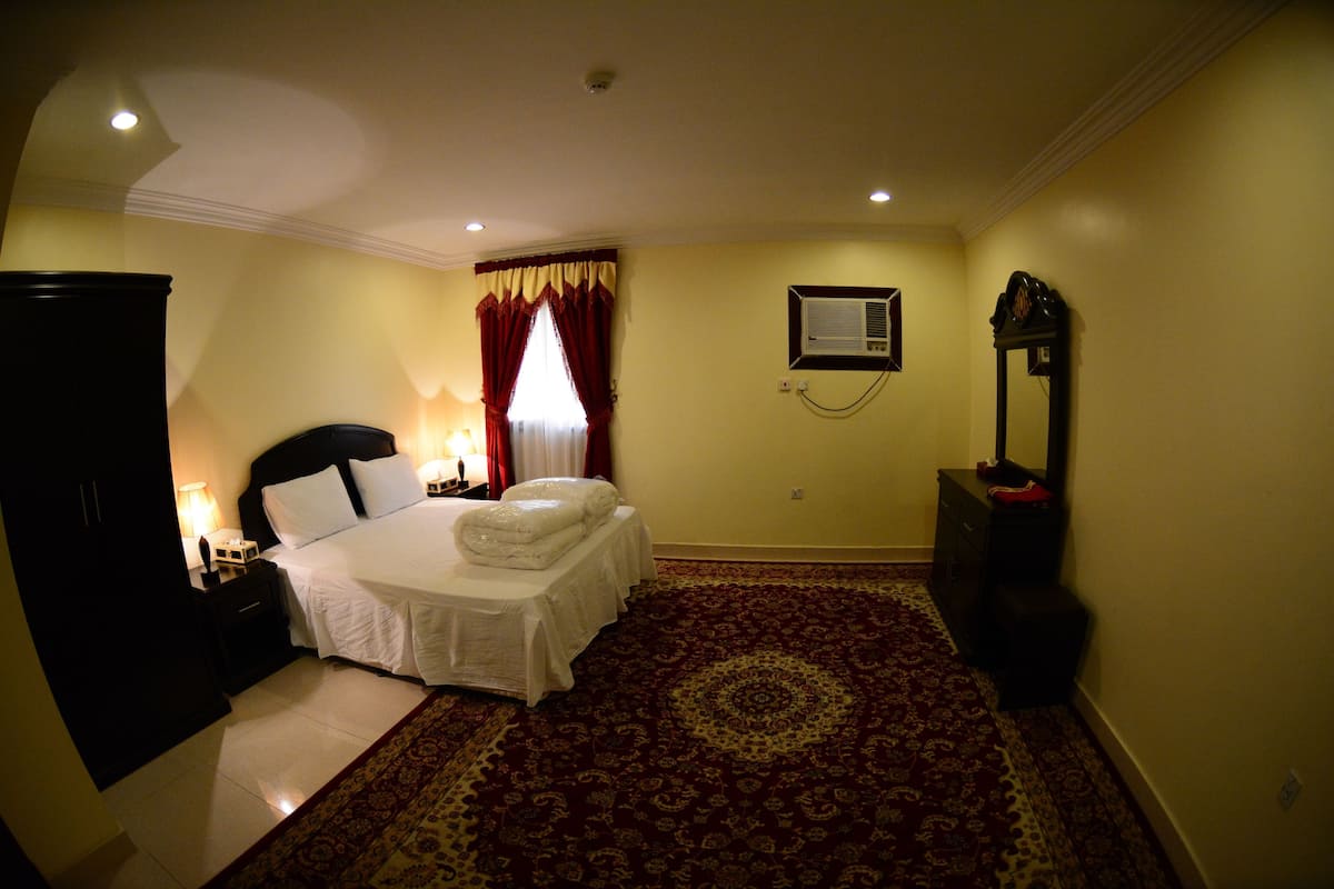 Habitación de hotel con cama, mesita de noche, lámpara, aire acondicionado y espejo.
