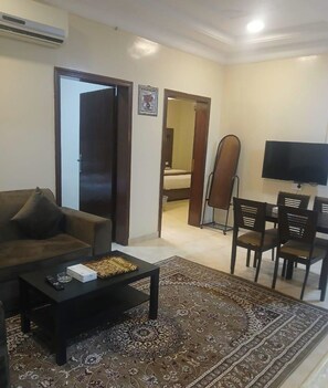 Uma sala de estar com sofá, mesa de centro, televisão e área de jantar com cadeiras.