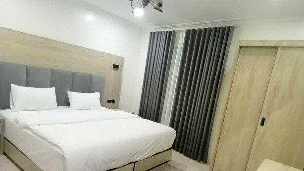 Une chambre moderne avec un grand lit, une armoire en bois et un tapis gris.