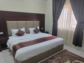A hotel room with a large bed, a wooden headboard, a nightstand, and a window with curtains. - Aleairy commercial group co ltd 4 (Dammam)