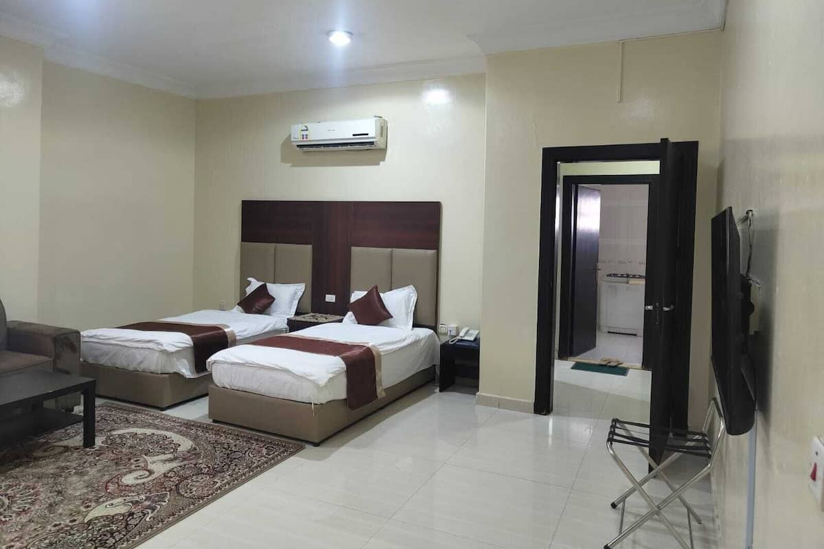 Habitación de hotel con dos camas, un sofá, un televisor y aire acondicionado.