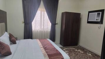 Habitación de hotel con cama, armario, ventana con cortinas y aire acondicionado instalado en la pared.