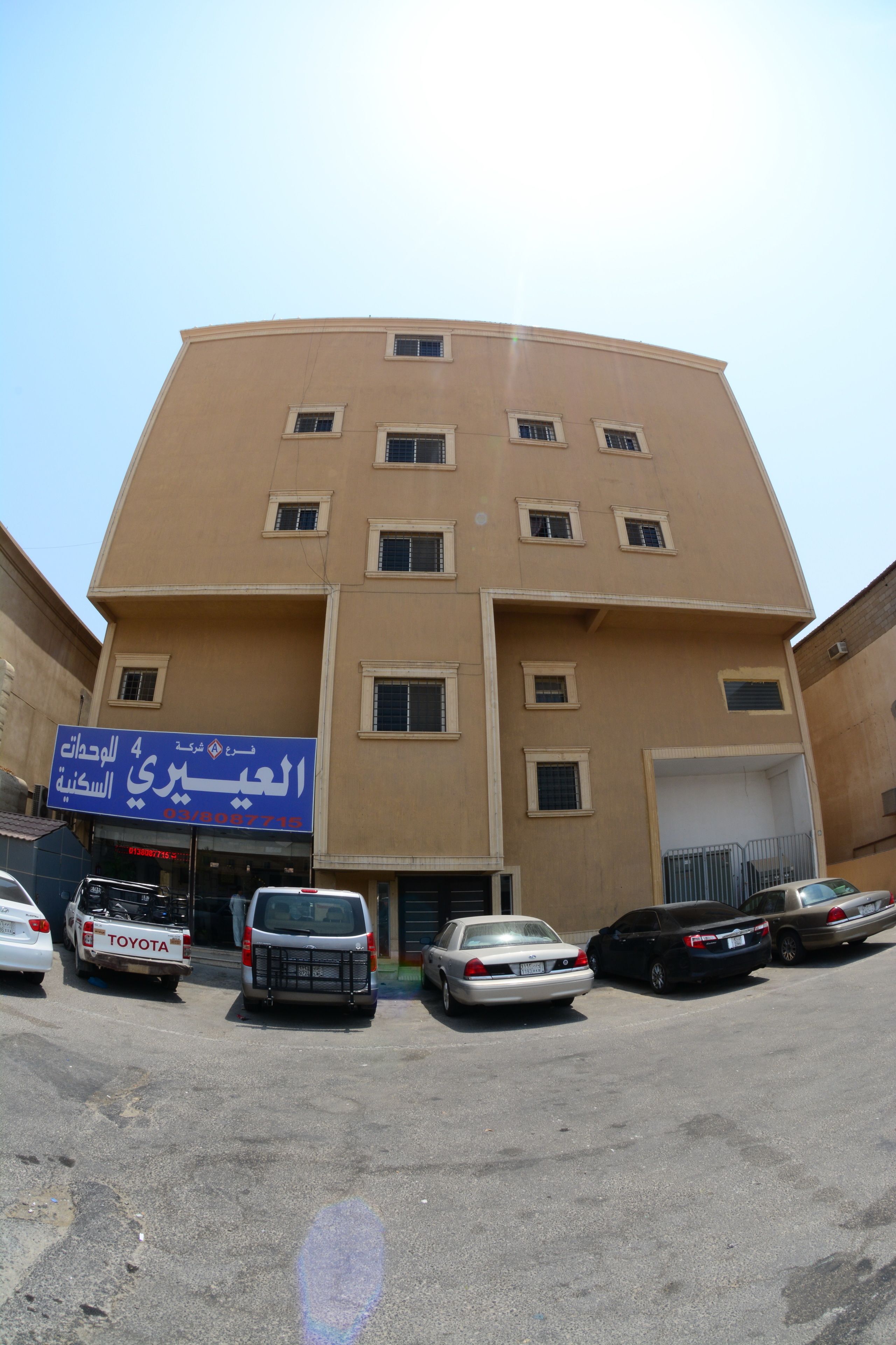 A multi-story building with a beige facade, several windows, and a signboard.