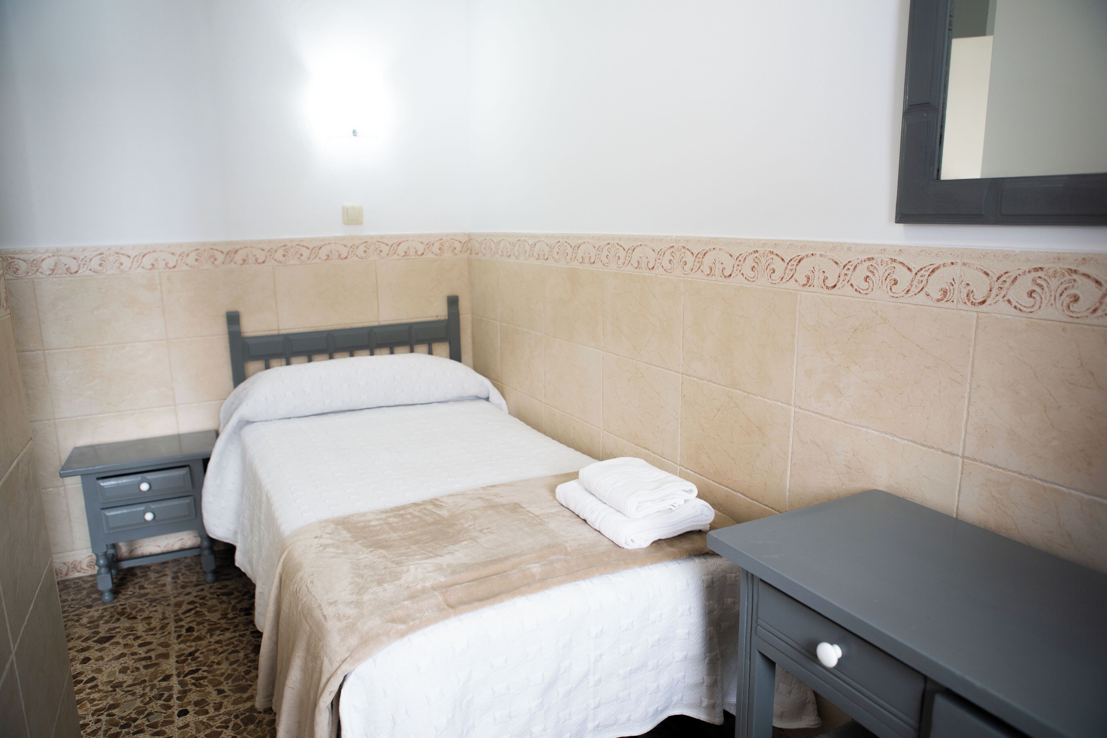 Une petite chambre à coucher, bien rangée, avec un lit, une table de chevet et une commode.
