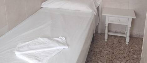 Habitació petita amb un llit individual, una nit i una làmpada de paret.
