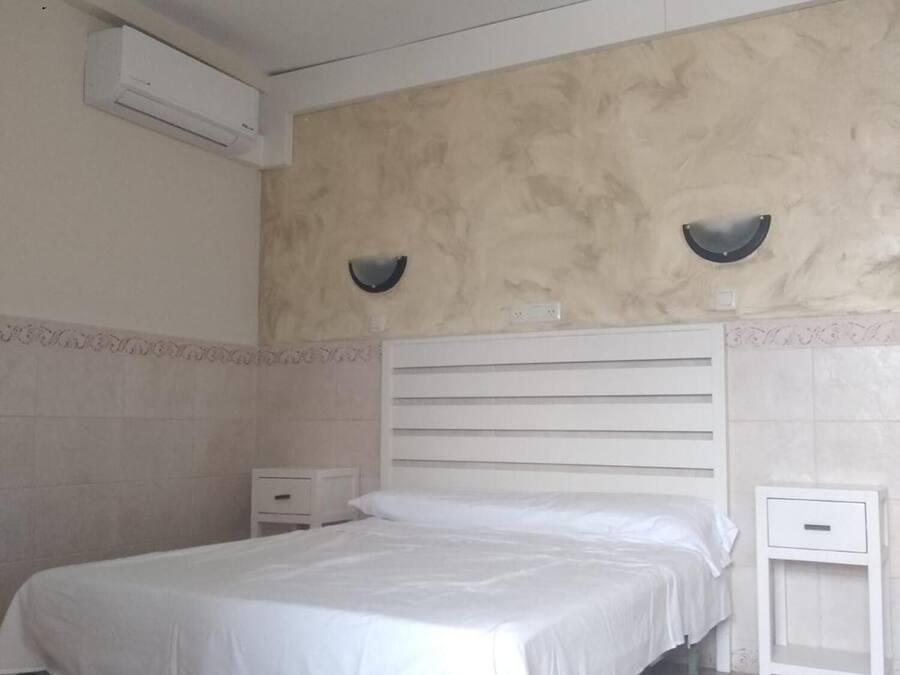 A bedroom with a bed, two bedside tables, an air conditioning unit, and a textured wall.