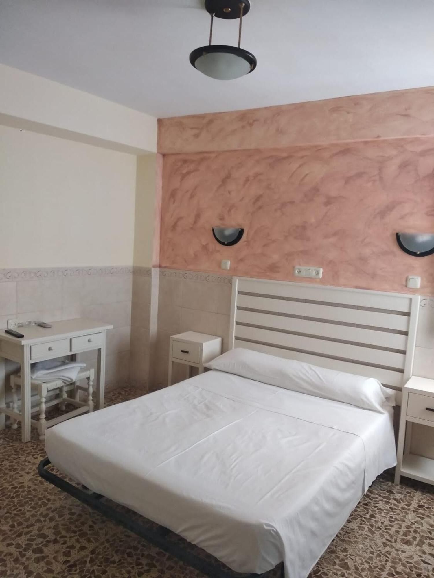 Un dormitorio con cama, mesitas de noche, espejo e iluminación en el techo.