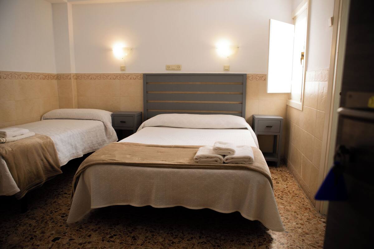 A hotel room with two beds, each with a headboard, bedside tables, and lamps.