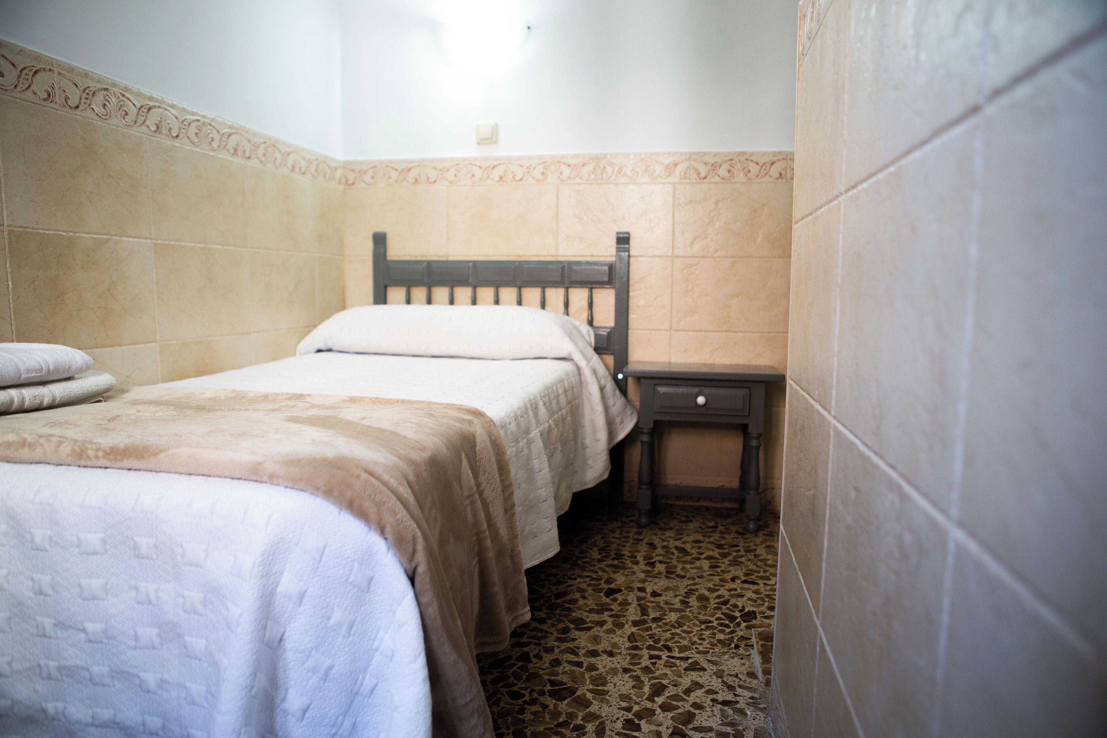 Une petite chambre à coucher, bien rangée, avec un lit simple, une table de chevet et une commode.