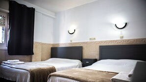 Habitación de hotel con dos camas, una cortina negra, un aplique de pared y una mesita de noche pequeña.