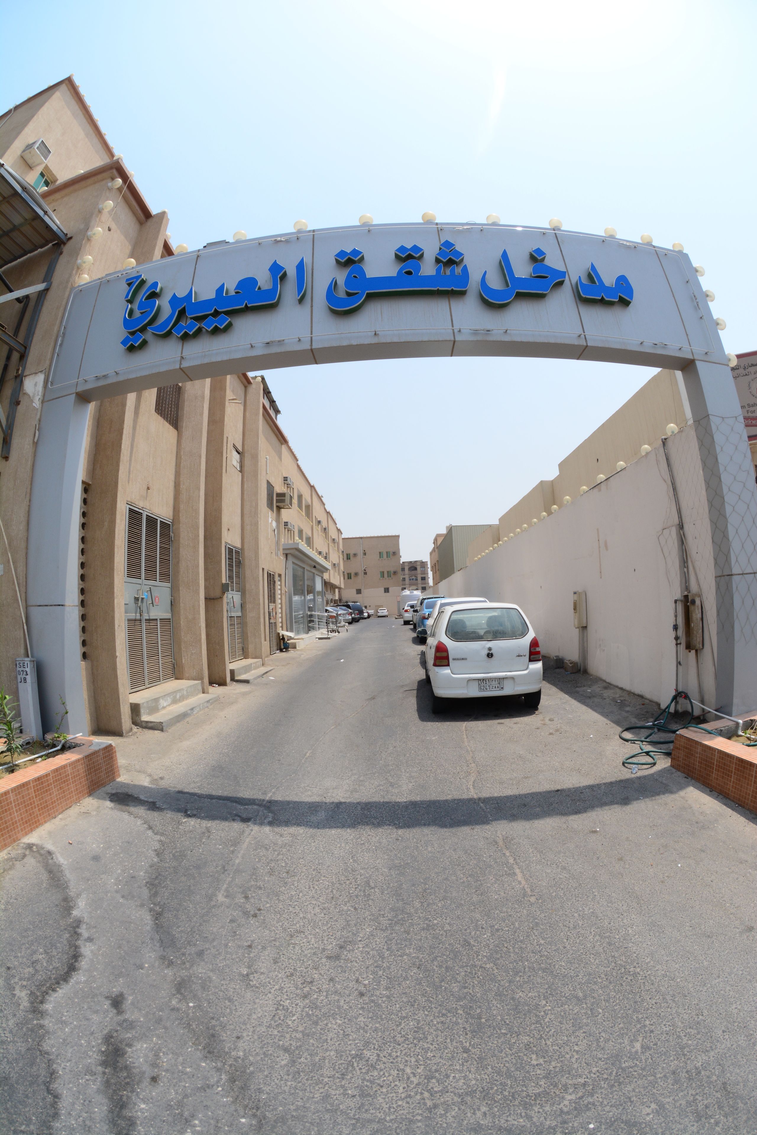 A street with a sign reading "ميدان الحي الكبير" and several parked cars.